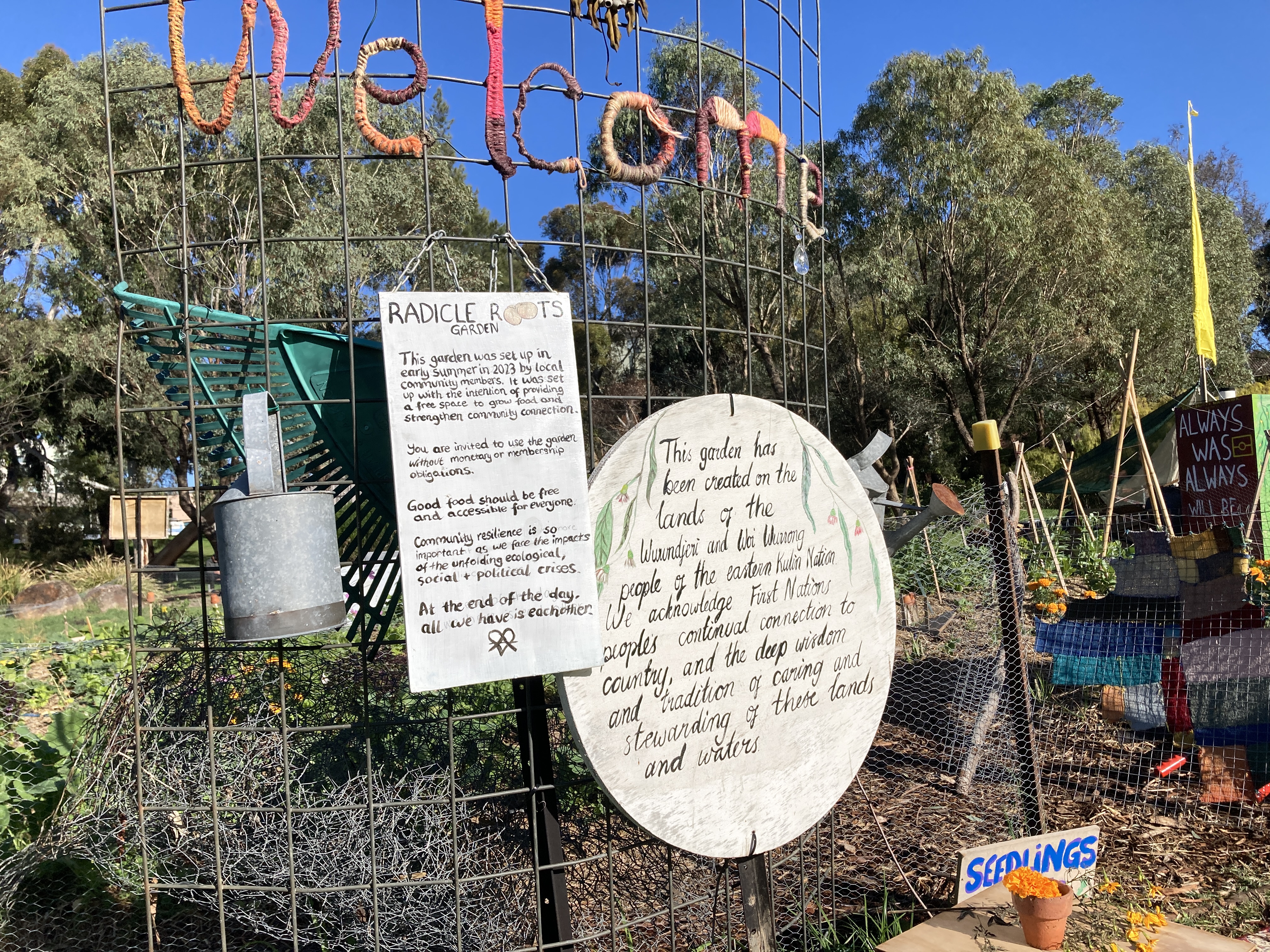 A picture of the entrance to the radical roots garden. A beautiful vegetable garden sitting behind a fence with hand painted signs. 