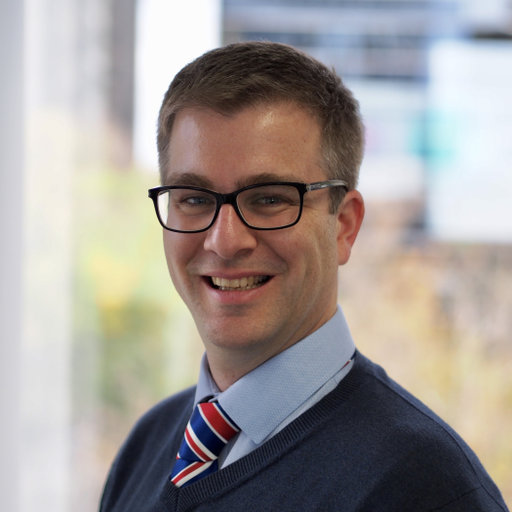 Luke Gahan man with short hair glasses dark blue sweater light bue shirt striped tie