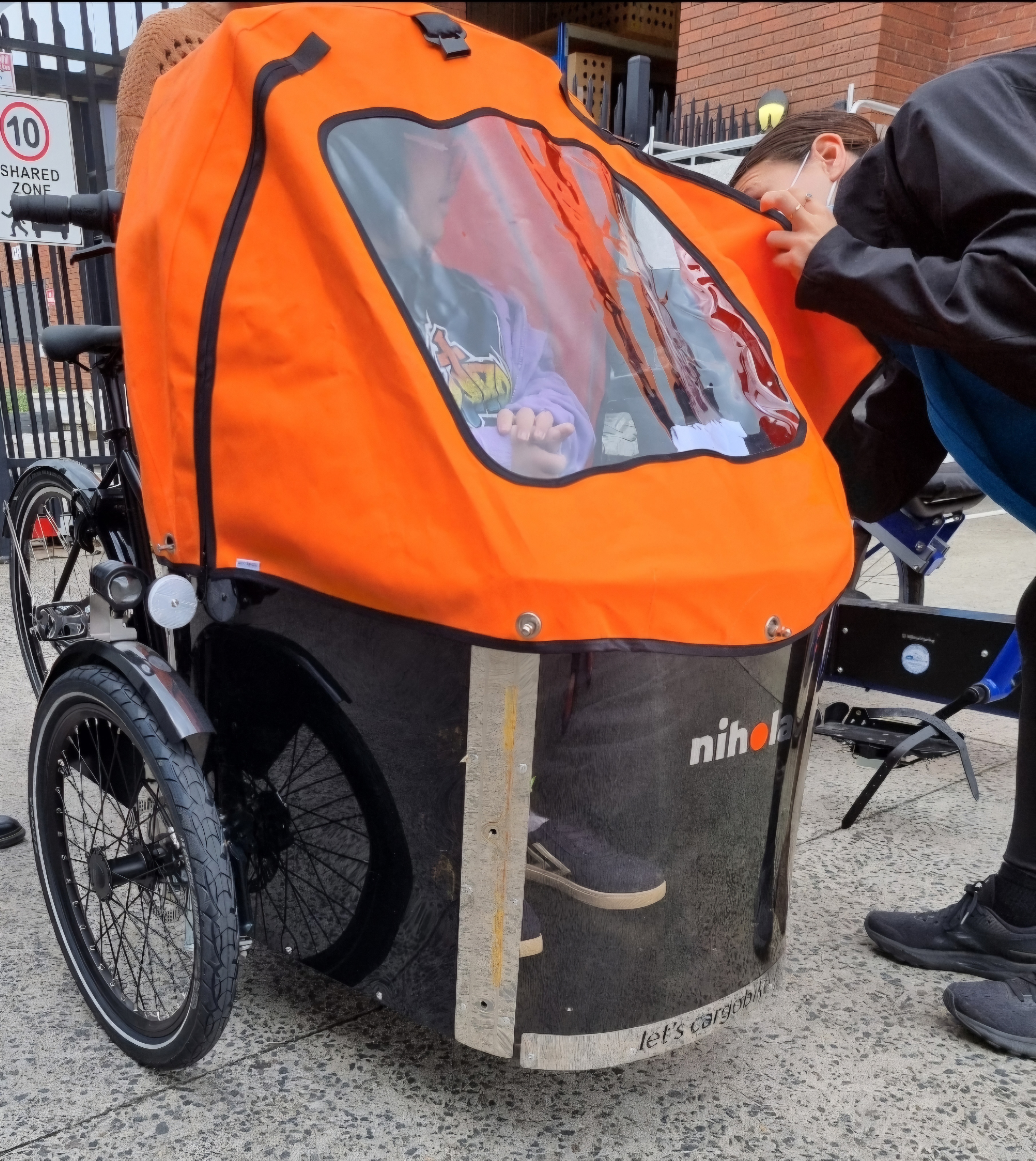 Christa (seated inside the cargobike) and her Sr Occupational Therapist standing beside the cargobike and peeking inside to checking on Christa. Image: supplied