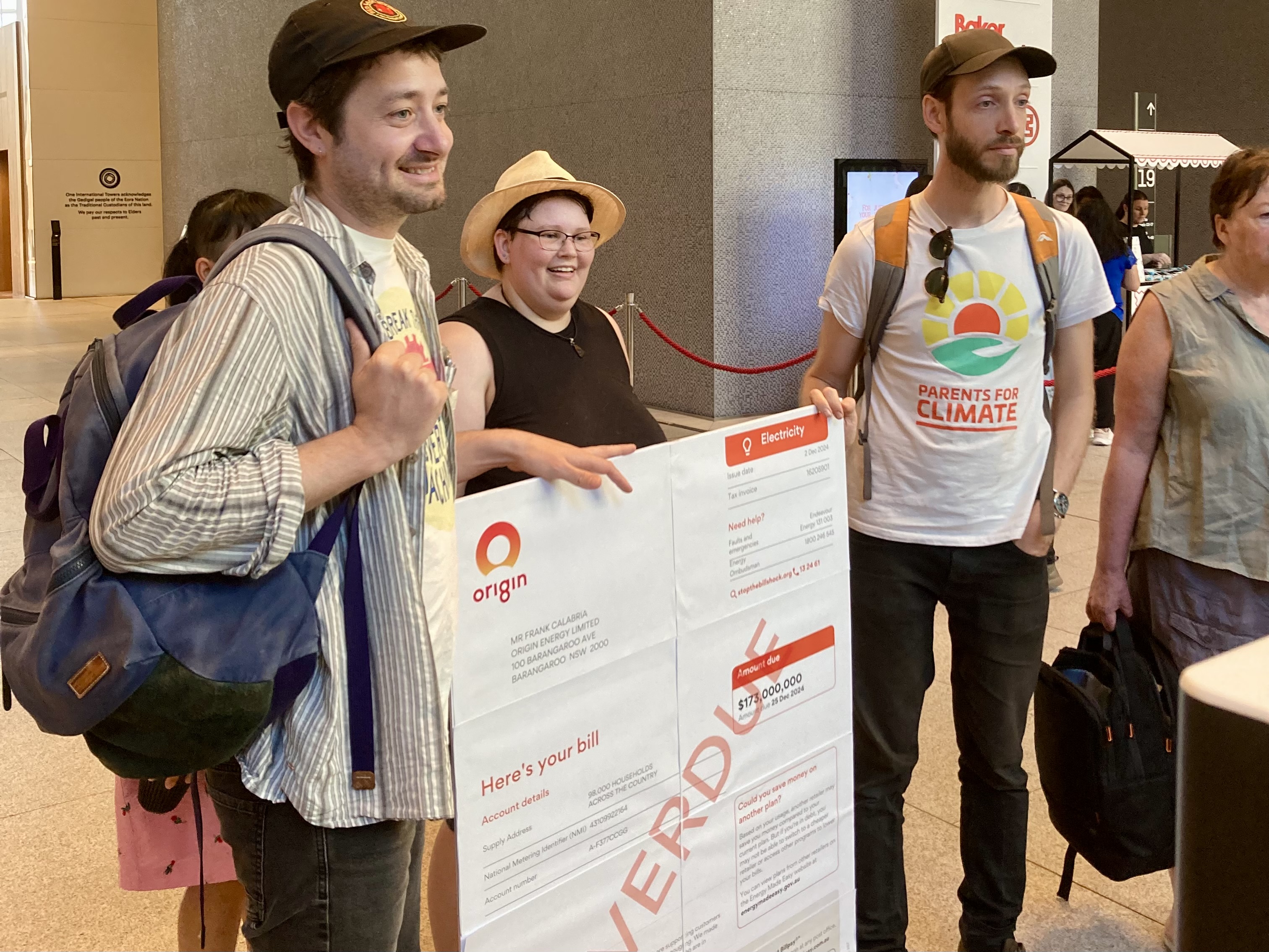 Three people holding an oversized mock Origin energy bill.