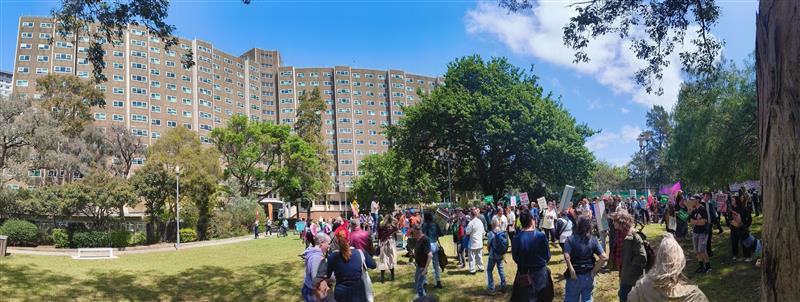 A wide shot of public housing towers at the Flemington estate and a crowd of people at the rally to save public housing.