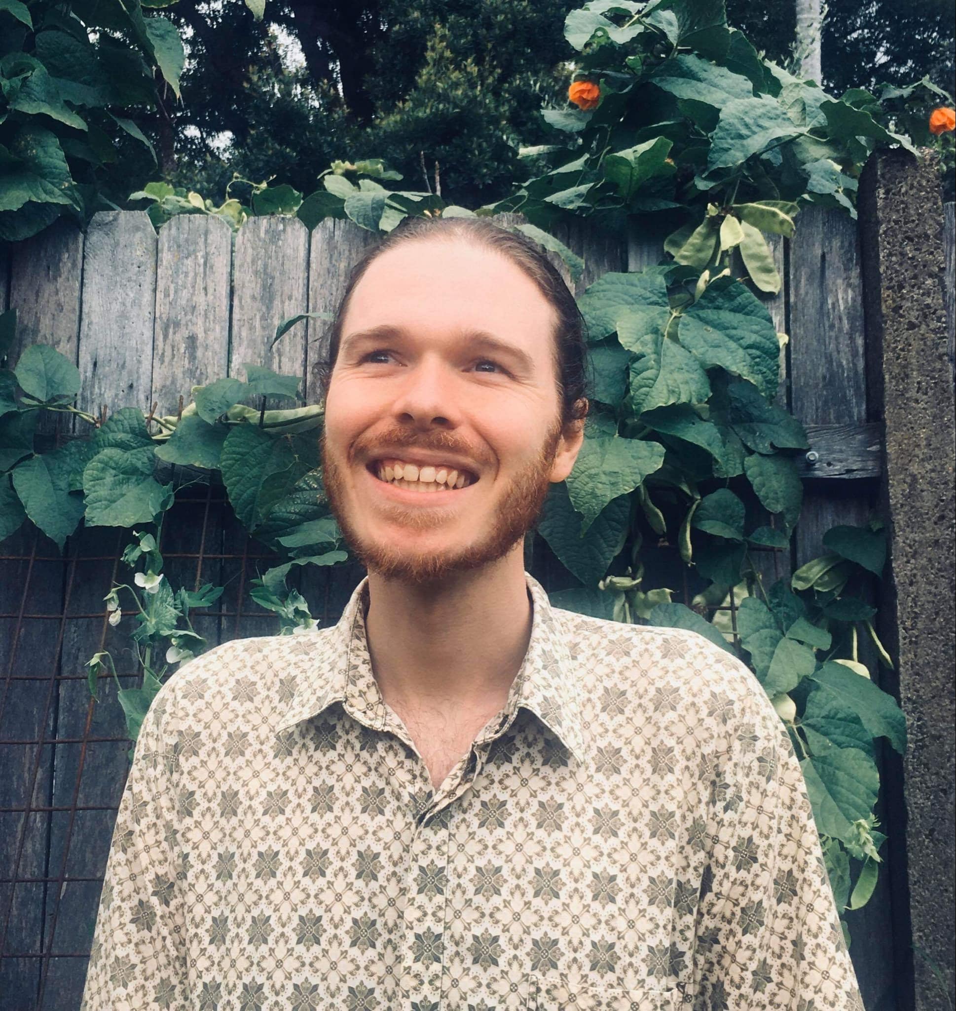 Alex Hill, smiling while standing in front of a garden fence