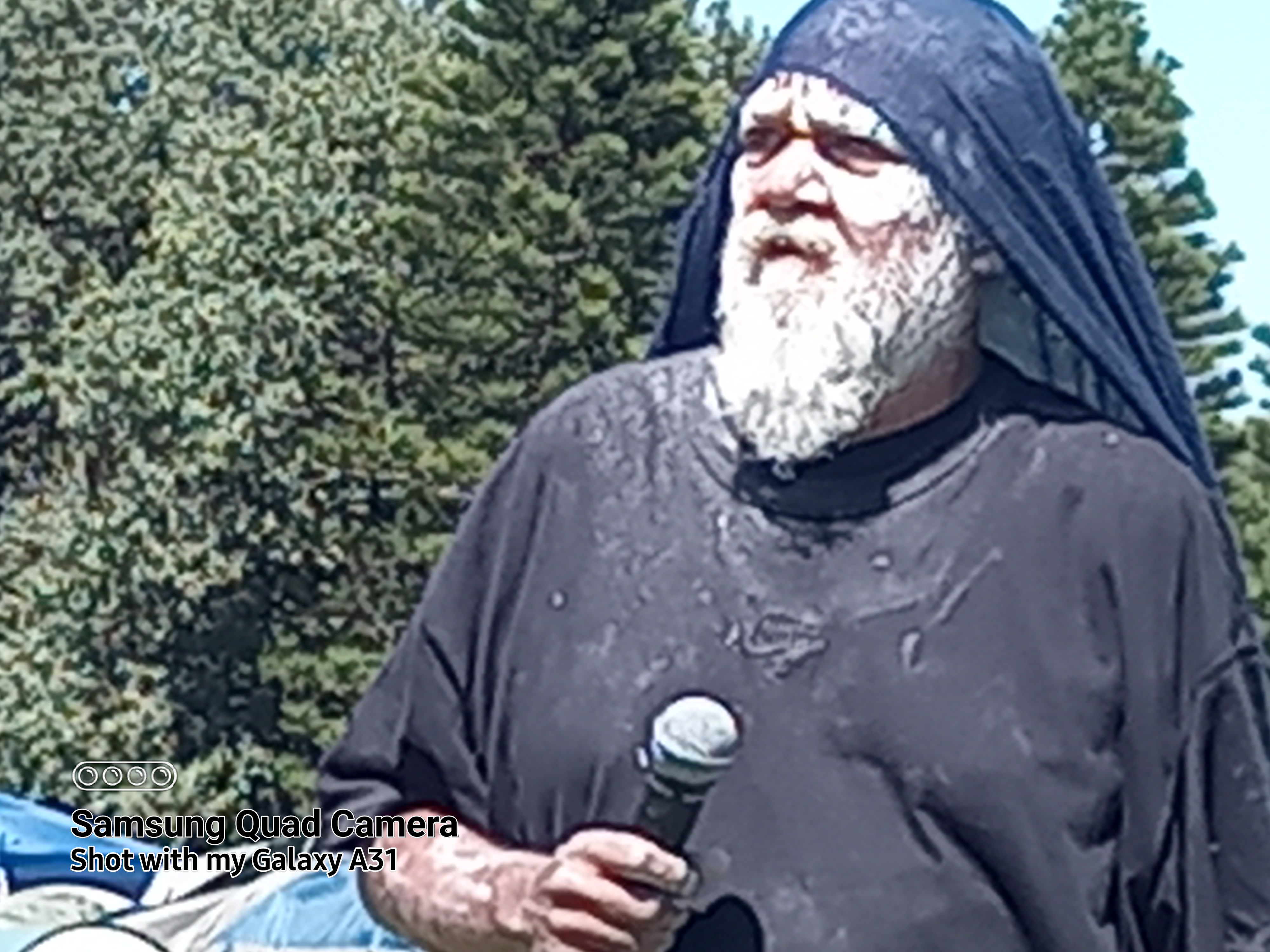 A First Nations elder man, with white paint face, black clothes and microphone