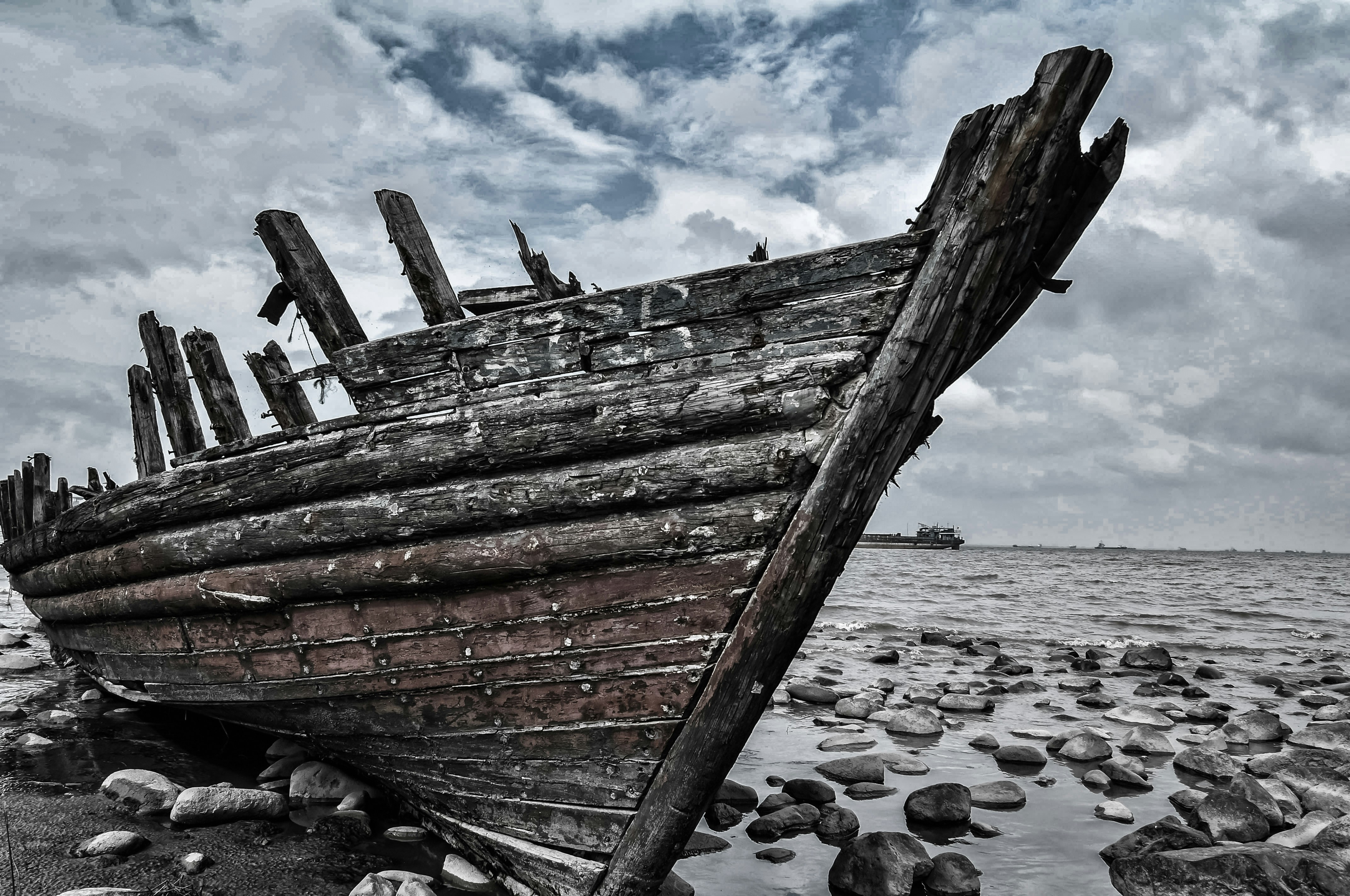 A decaying timber boat hull, stranded on a rocky sea shore