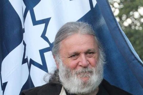 Image of Joe Toscano, a man with a full grey hair, beard and moustache, in warm winter clothes, carrying a Eureka Stockade Flag.