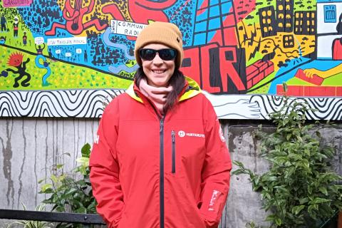 Sally stand in the 3CR wearing her kit from Antartica: a red windbreaker, snow goggles and beanie.