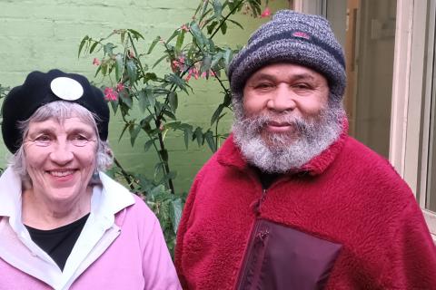 Jacob and Louise stand in the 3CR courtyard. They are wearing their winter woolies in pink and red, complete with beret and beanie.