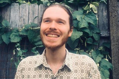 Alex Hill, smiling while standing in front of a garden fence