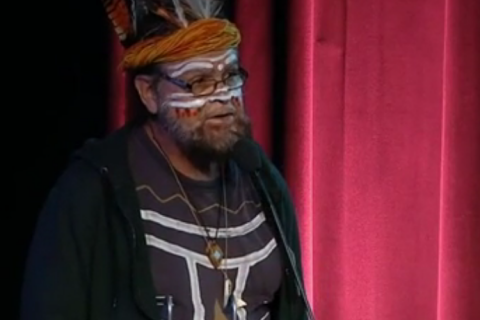 Uncle Bunna Lawrie in full face paint & t-shirt with body paint, and with ceremonial head dress & feathers at Equinor AGM