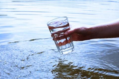 A glass of water held by a hand above a body of water
