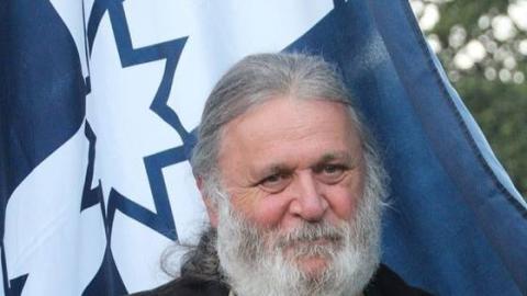 Image of Joe Toscano, a man with a full grey hair, beard and moustache, in warm winter clothes, carrying a Eureka Stockade Flag.