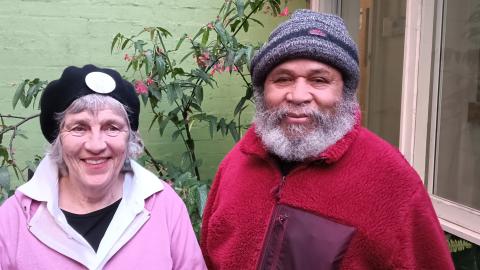 Jacob and Louise stand in the 3CR courtyard. They are wearing their winter woolies in pink and red, complete with beret and beanie.